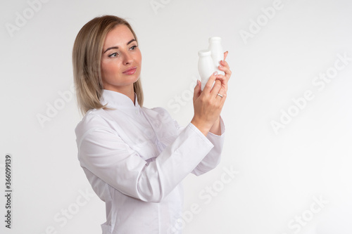 Cosmetology woman. Woman beautician in a white shirt. Blonde. Girl beautician examines some bottles. Casmetologist examines a white tube. Concept - she works in the field of cosmetology.