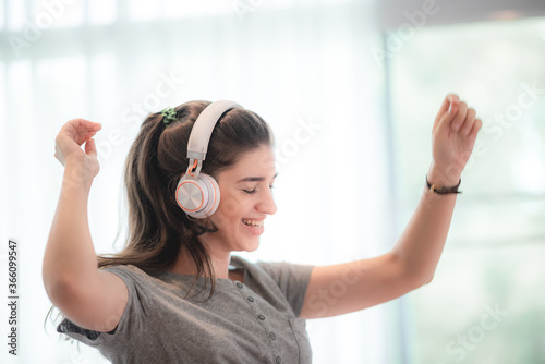 Happy young woman in headphones is listening to music, relax dancing and smiling in bedroom at home