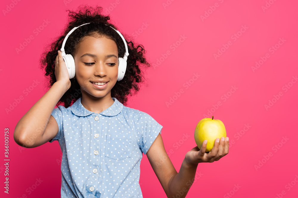 smiling curly african american kid in headphones holding apple isolated on pink smiling curly african american kid in headphones holding apple isolated on pink