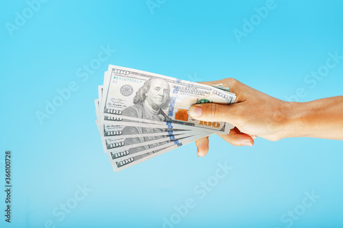 A hand with one hundred-dollar bills on a blue background.