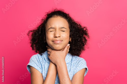 curly african american kid with closed eyes and hands on throat isolated on pink photo
