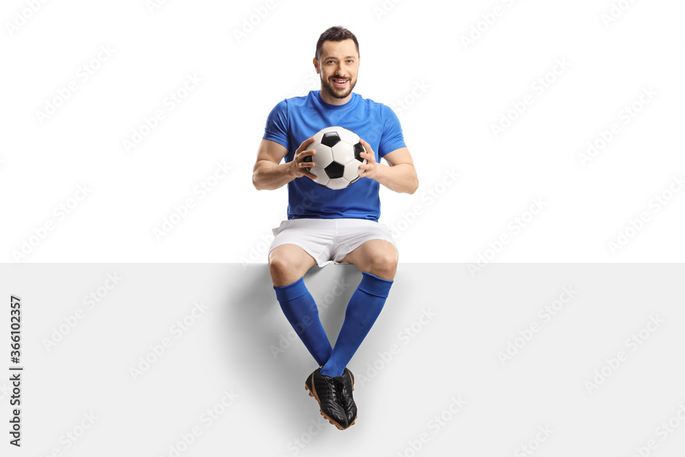 Footballer sitting on a blank panel and holding a soccer ball