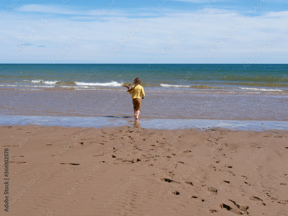 girl on the beach walking away towards the water girl on the beach walking away towards the water