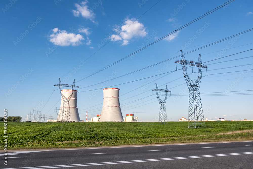Cooling towers of nuclear power plant with high voltage electric pylon towers against the blue sky Cooling towers of nuclear power plant with high voltage electric pylon towers against the blue sky