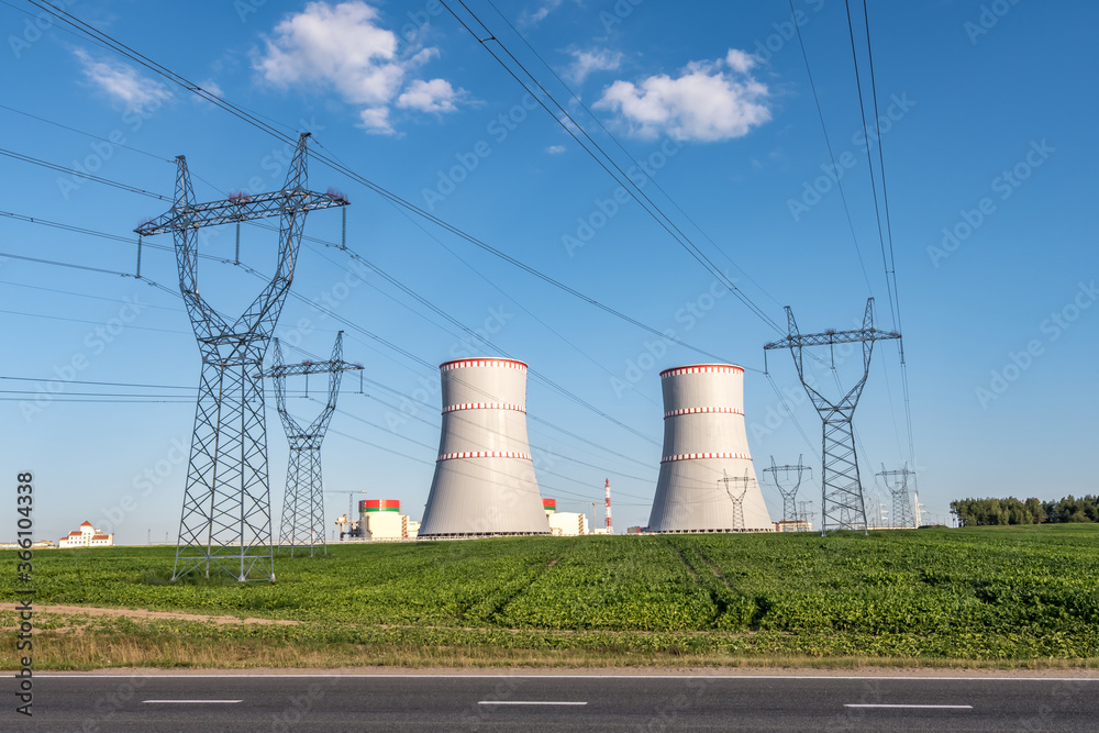 Cooling towers of nuclear power plant with high voltage electric pylon towers against the blue sky