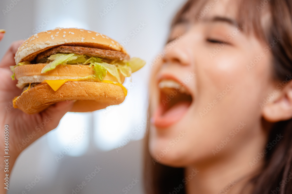 Hungry young woman eating junk food hamburger and pizza for lunch by ordering delivery at home on holiday. unhealthy meal, obesity risk. Hungry young woman eating junk food hamburger and pizza for lunch by ordering delivery at home on holiday. unhealthy meal, obesity risk.