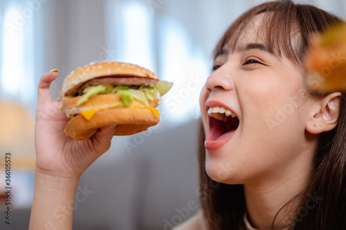 Hungry young woman eating junk food hamburger and pizza for lunch by ordering delivery at home on holiday. unhealthy meal, obesity risk.