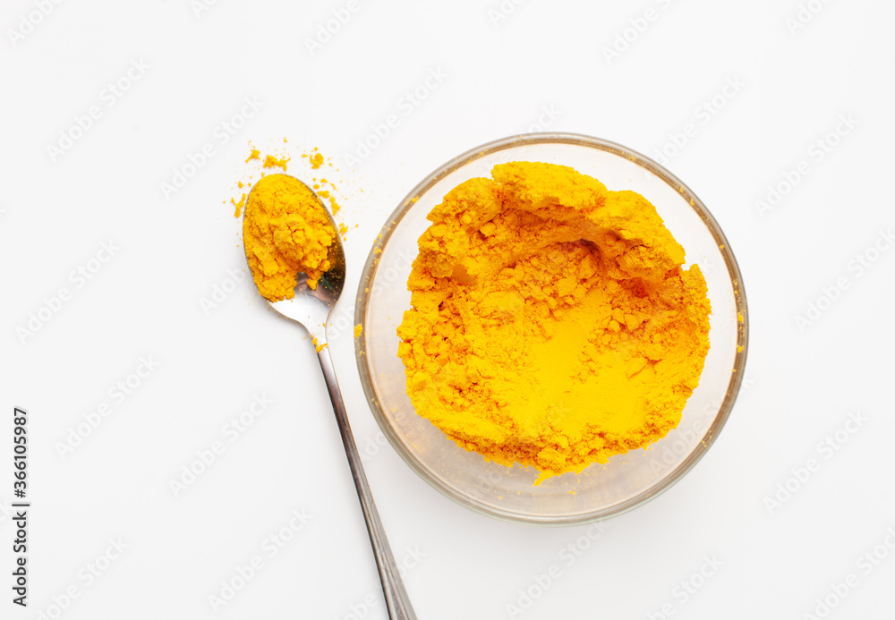 Ground turmeric root in powder in a bowl and next to scattered in a spoon Ground turmeric root in powder in a bowl and next to scattered in a spoon