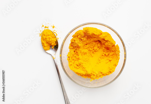 Ground turmeric root in powder in a bowl and next to scattered in a spoon