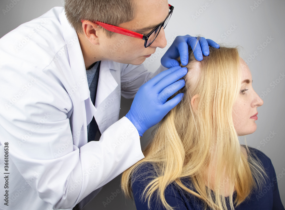 A doctor trichologist conducts a study of the hair of a blonde. Alopecia treatment. Hair loss, alopecia, itching, burning in the head, seborrhea or brittle ends A doctor trichologist conducts a study of the hair of a blonde. Alopecia treatment. Hair loss, alopecia, itching, burning in the head, seborrhea or brittle ends