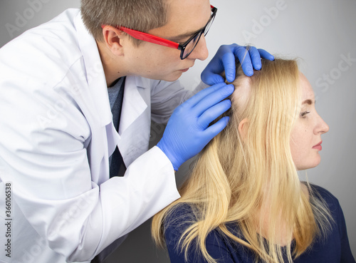 A doctor trichologist conducts a study of the hair of a blonde. Alopecia treatment. Hair loss, alopecia, itching, burning in the head, seborrhea or brittle ends