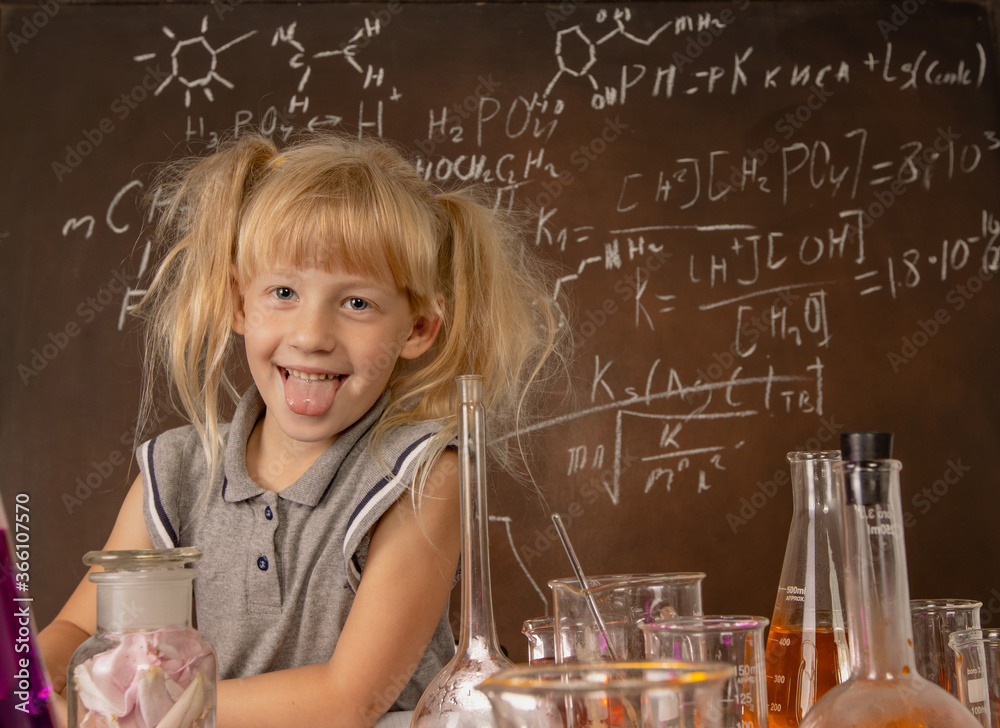 Curious little girl with test tubes and colorful substances making tests anf keeping her toungue ou at school laboratory. Small kid learning chemistry and conducts science experiment on biology lesson