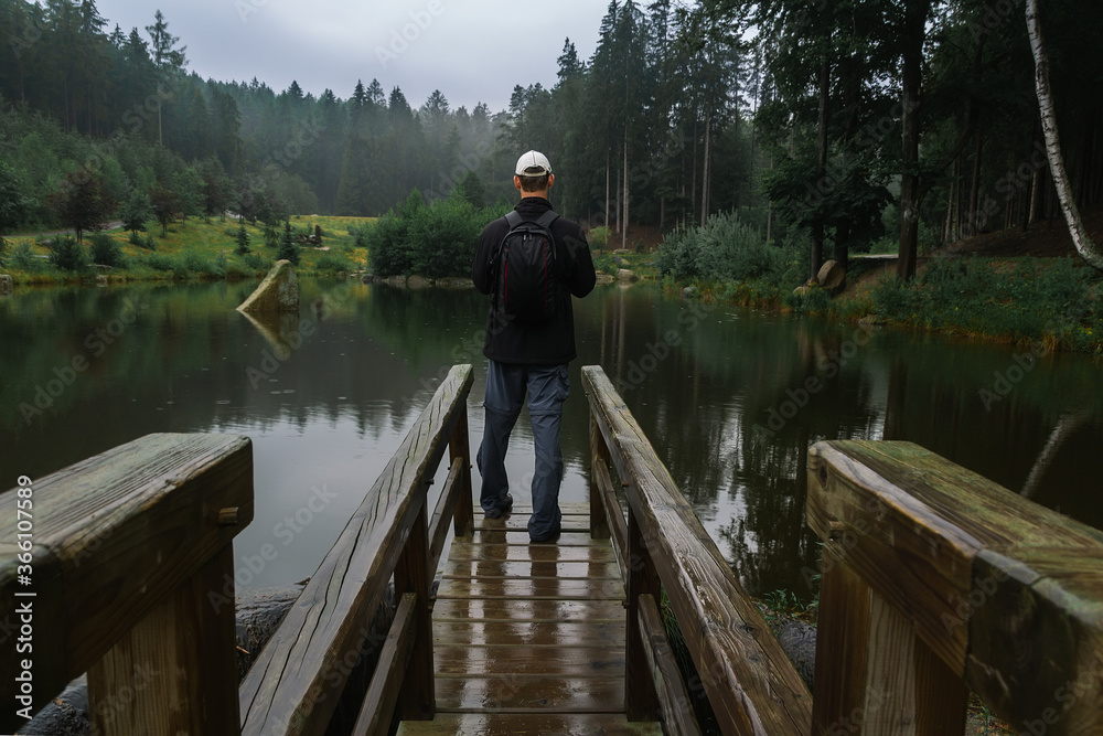 Young man standing on loodgate pond in rainy weather. Natural reserve Czech canada, dark mood green