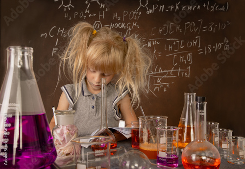 Curious little girl with test tubes and colorful substances making tests and taking notes at school laboratory. Small kid learning chemistry. Biology education concept.