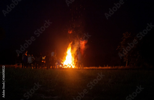 People relax on a holiday in the forest near a large bonfire at night. National holiday background, copy space