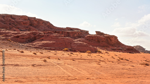 Rocky massifs on red sand desert, bright cloudy sky in background - typical scenery in Wadi Rum, Jordan