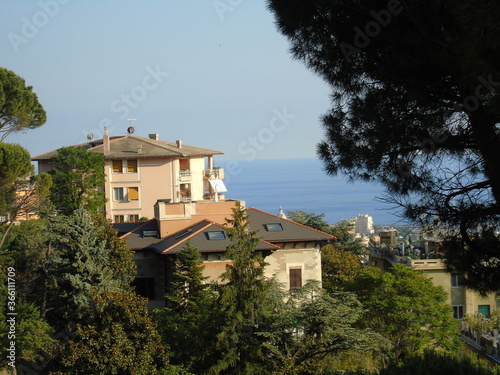 Genova, Italy - 07/12/2020: An amazing photography of the city of Genova from the hills in summer days, with a great blue sky in the background and some trees behind the buildings.