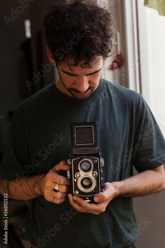 Portrait shot of a film photographer on a indoors shooting using an old medium format brand less camera.