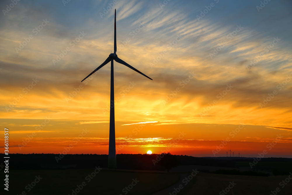 Obraz premium Sunny sunset with beautiful clouds and windmill silhouette