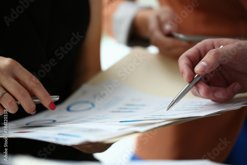 Close up cropped head of male and female hands with economic chart and pens while people are discussing document
