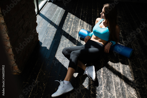 Top view of a girl lying on a foam massage cylinder for working out the fascia muscles and looking towards the light on the floor in a loft