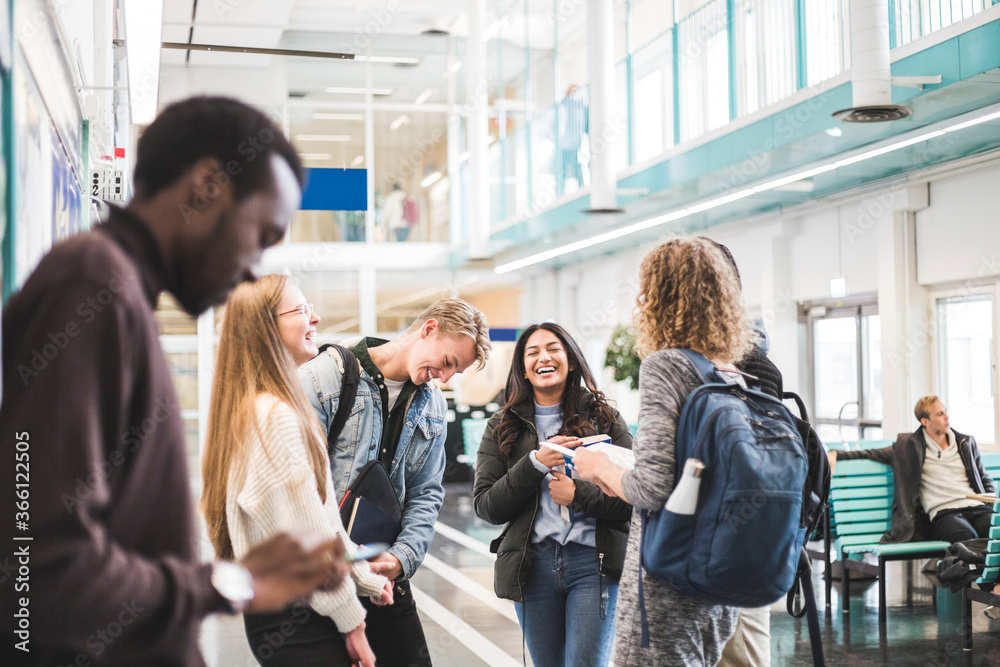 Cheerful young male and female students talking while standing in cafeteria at university Cheerful young male and female students talking while standing in cafeteria at university