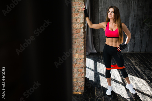 Full length portrait of a woman exercising her inner thighs and legs using a sports elastic expander in a loft © DmitryStock