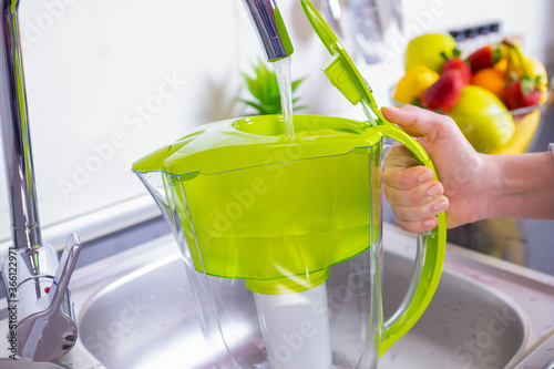 Obraz na płótnie Woman filling water filter jug in the kitchen