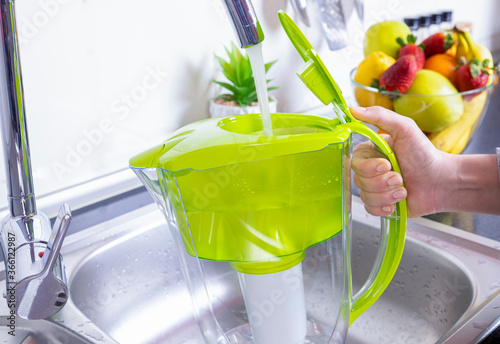 Woman filling water filter jug in the kitchen photo