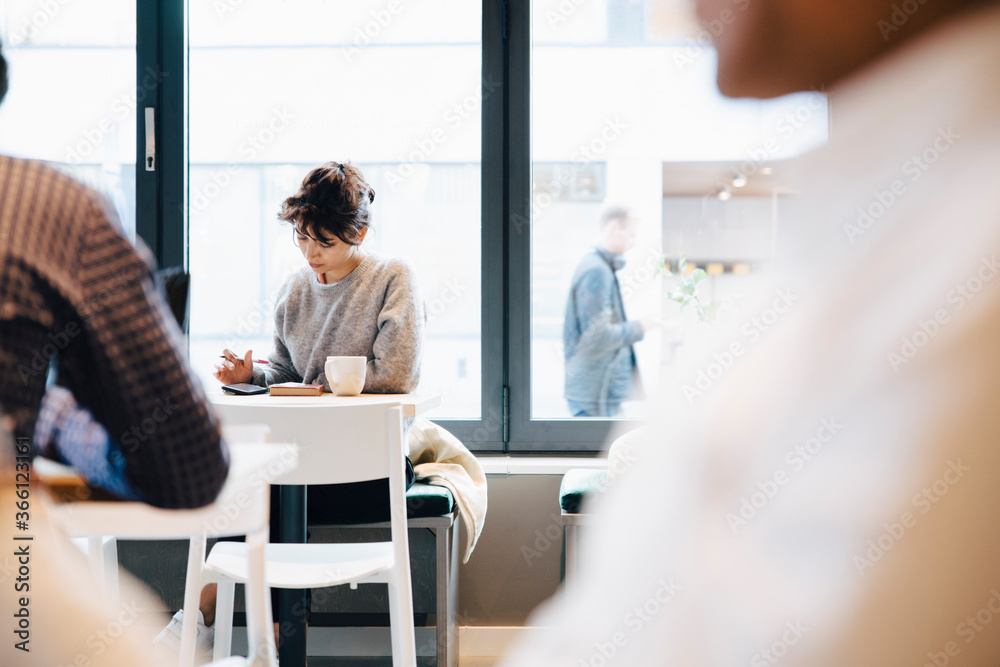 Female customer using mobile phone while sitting with coffee cup at table in cafe Female customer using mobile phone while sitting with coffee cup at table in cafe