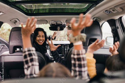 Cheerful family raising hands while enjoying road trip in electric car photo