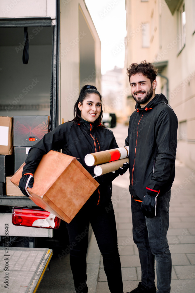 Portrait of confident young delivery man and woman with packages standing against truck in city Portrait of confident young delivery man and woman with packages standing against truck in city