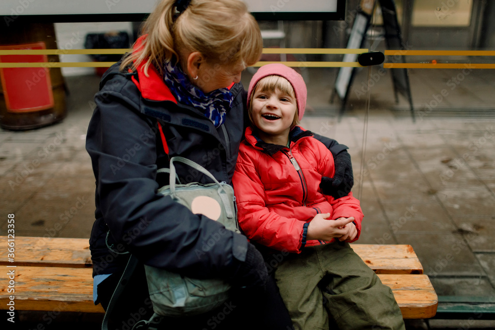Grandmother with smiling grandson sitting on bench in city Grandmother with smiling grandson sitting on bench in city