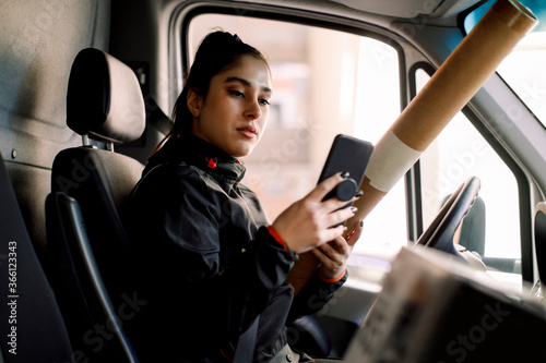 Young delivery woman using smart phone while holding package in truck photo