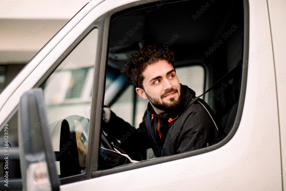 Young delivery man looking through window while driving truck Young delivery man looking through window while driving truck