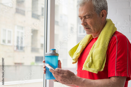 man doing sports with towel and bottle of water using mobile phone