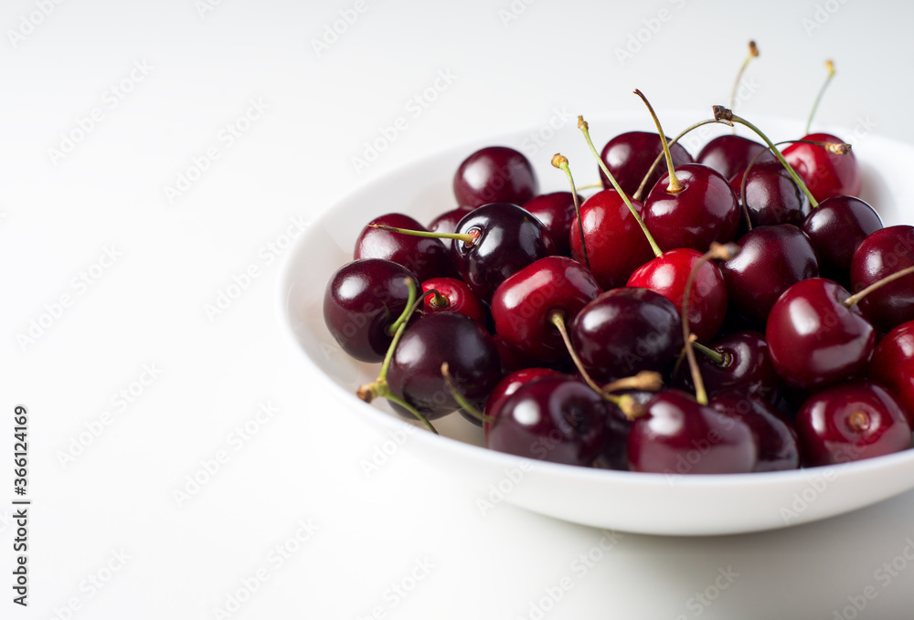 Cherry in white dish. A bunch of juicy ripe sweet cherries in a white plate on a white background. Fresh red berries contrast with the white table. Cherry in white dish. A bunch of juicy ripe sweet cherries in a white plate on a white background. Fresh red berries contrast with the white table.