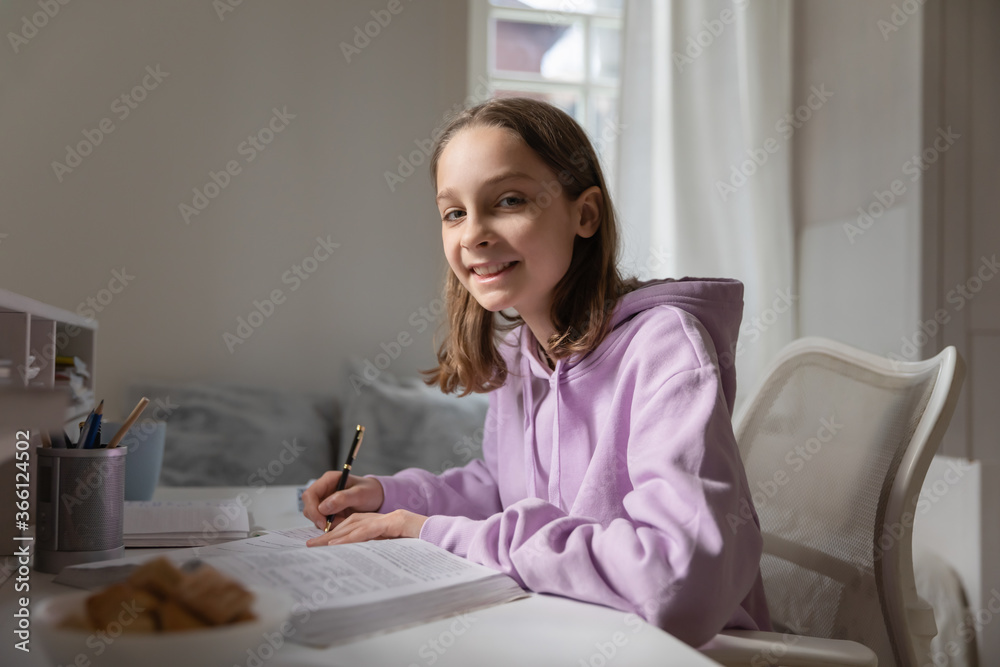 Head shot portrait smiling teenage girl studying at home, teen schoolgirl doing school assignments, homework, writing essay or notes, preparing for exam, sitting at desk, looking at camera Head shot portrait smiling teenage girl studying at home, teen schoolgirl doing school assignments, homework, writing essay or notes, preparing for exam, sitting at desk, looking at camera