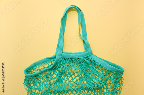 Cotton green smesh bag on yellow paper background. Eco-friendly shopping without plastic