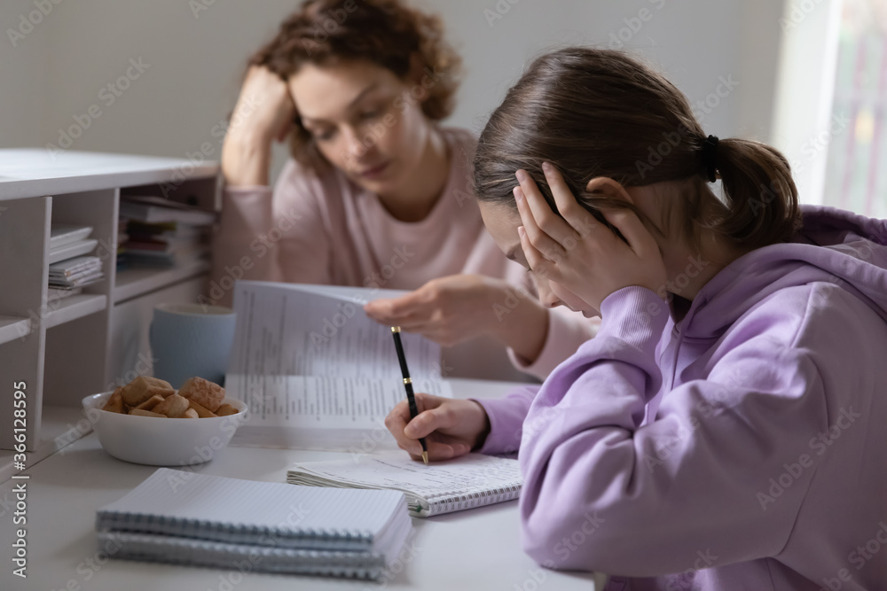 Upset mother and teenage daughter studying at home, sad unhappy teen girl doing school assignments, difficult task, routine boring homework, strict mother controlling lazy schoolgirl Upset mother and teenage daughter studying at home, sad unhappy teen girl doing school assignments, difficult task, routine boring homework, strict mother controlling lazy schoolgirl