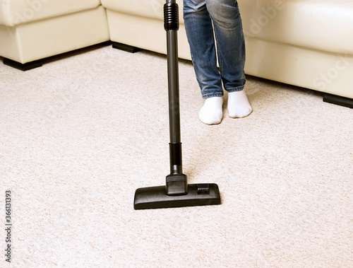 girl in jeans vacuuming the house. bright carpet and light leather sofa photo