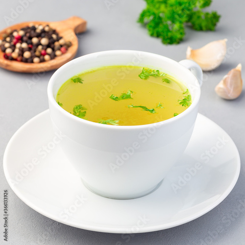 Chicken broth in white cup with chopped parsley, square format