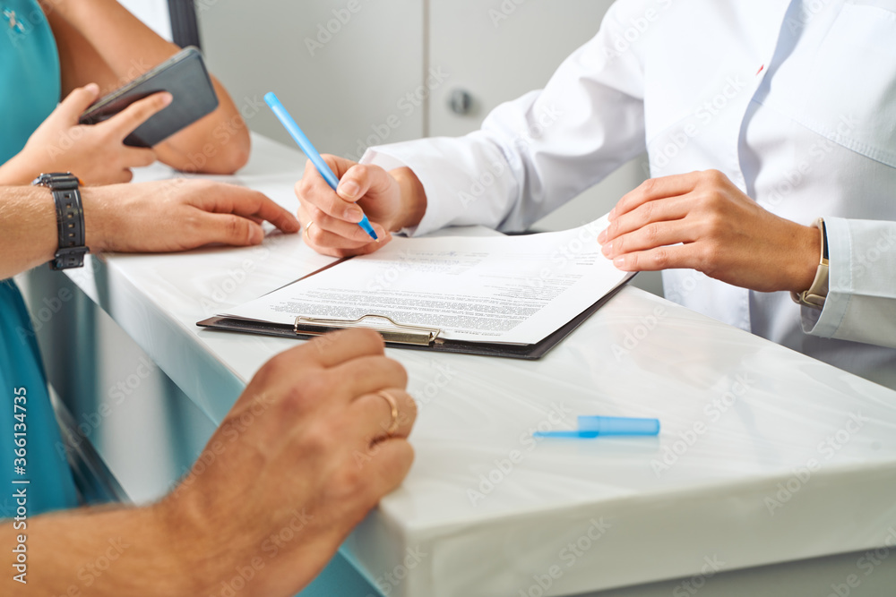 Partial view of doctor in white coat making notes in notepad with female patient near by during appointment in clinic Partial view of doctor in white coat making notes in notepad with female patient near by during appointment in clinic