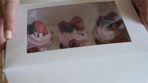 Process of packing fruit cupcakes in a white cardboard box. Preparing a sweet dessert for delivery.