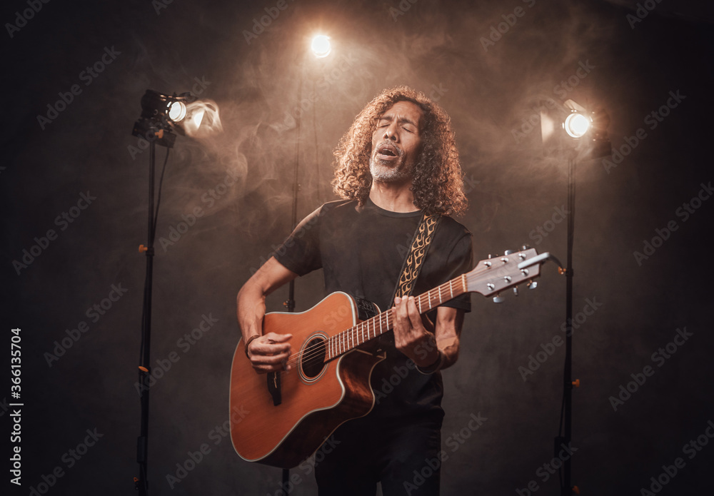 Talented hispanic musician in black t-shirt playing guitar. View of musician in the spotlight Talented hispanic musician in black t-shirt playing guitar. View of musician in the spotlight