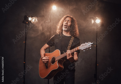 Talented hispanic musician in black t-shirt playing guitar. View of musician in the spotlight