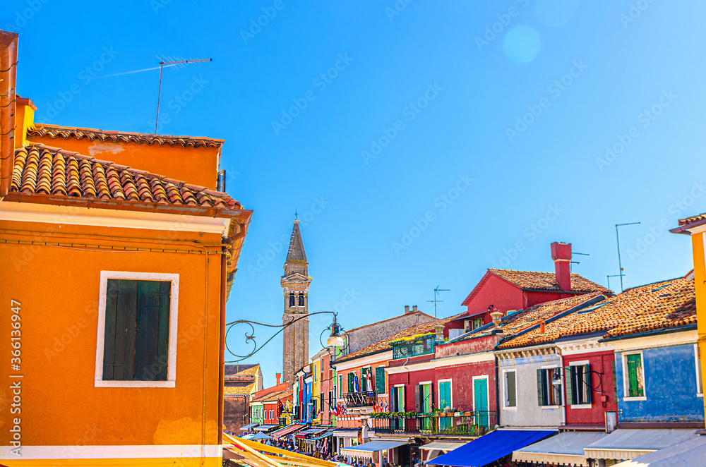 Top roofs of colorful houses with multicolored walls and Bell tower of San Martino church in Burano island, blue sky in sunny summer day background, Venice Province, Veneto Region, Northern Italy