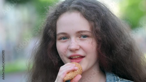 Pretty European teen girl eating ice cream walking on city street