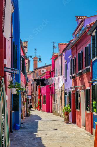 Burano island narrow cobblestone street between colorful houses buildings with multicolored walls and clothes hanging on clothes line, vertical view, Venice Province, Veneto Region, Northern Italy