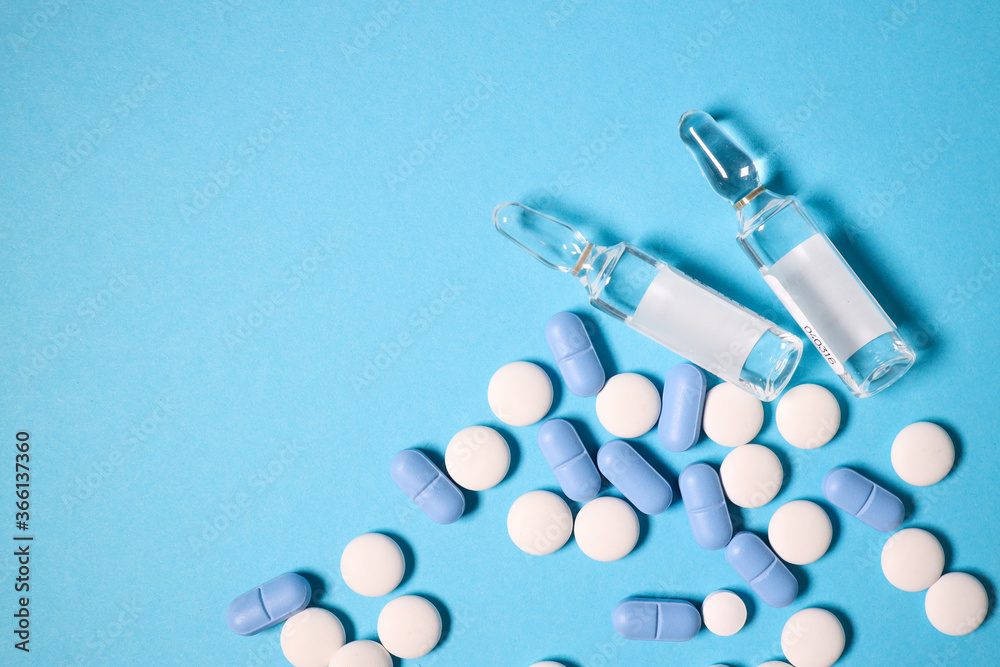 Transparent ampoules with liquid medicine are on blue background around tablets which form polka dots pattern. Concept photo of complex injection and pharmacological treatment of diseases, diversity Transparent ampoules with liquid medicine are on blue background around tablets which form polka dots pattern. Concept photo of complex injection and pharmacological treatment of diseases, diversity